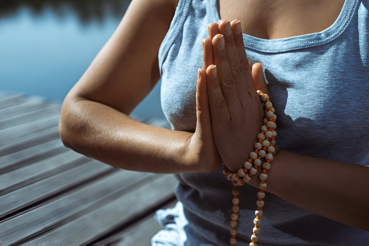 The young woman sitting on a wooden pier with her hands folded with a rosary in a prayer pose. Meditation, yoga in nature. Close-up.